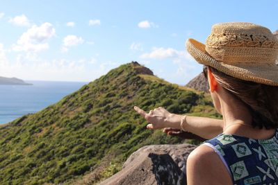 Rear view of woman looking at sea by mountain against sky