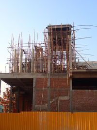 Low angle view of cranes against building against clear sky