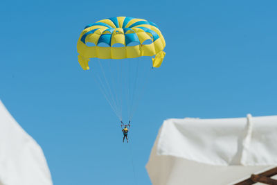 Low angle view of people paragliding against clear blue sky