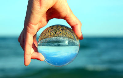 Close-up of hand holding crystal ball against sea