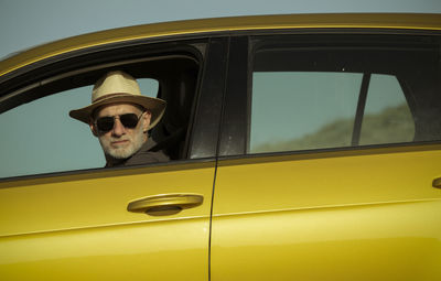 Adult man in hat and sunglasses sitting in car against clear sky