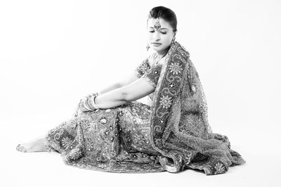 Young woman looking away while sitting against white background