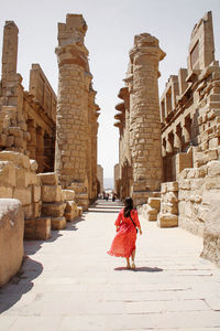 Woman with waving red dress walking through the ruins of the temple of karnak