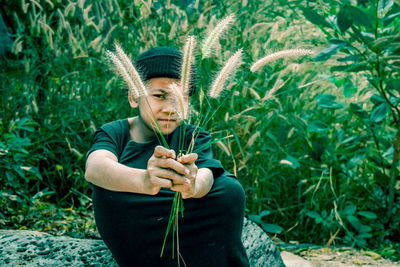 Portrait of boy holding flowers while sitting against plants