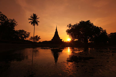 Silhouette temple by trees against orange sky