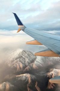 Close-up of airplane wing over landscape against sky