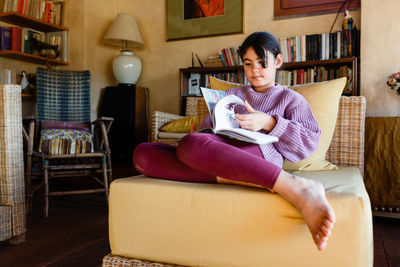 Smiling girl with dark hair flipping the pages of a book sitting in armchair