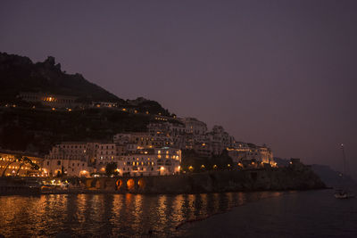 Illuminated buildings by river against sky at night