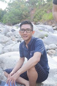 Portrait of smiling young man sitting on rock