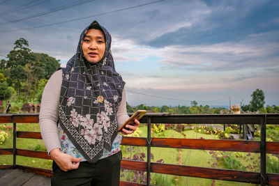 Portrait of young woman standing against sky