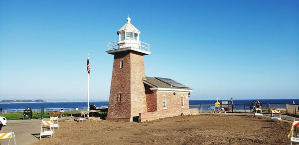 Lighthouse by sea against clear sky