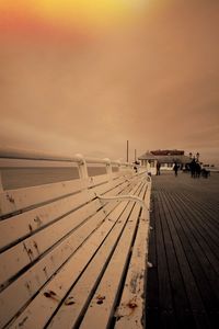 Empty bench on pier against cloudy sky during sunset