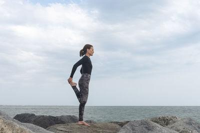 Sporty female doing a leg stretch, warm up exercises by the sea.