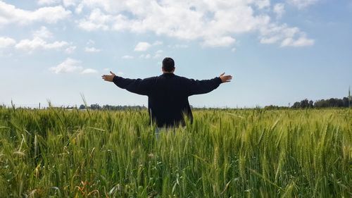 Rear view of man with arms outstretched standing on field against sky