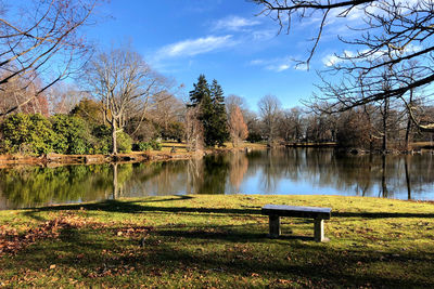 Empty bench by lake against sky