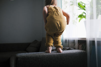 Child jumps and plays on sofa in minimalist living room, gray sofa.