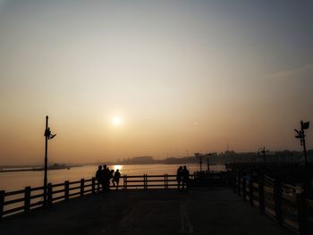 Silhouette people on pier by sea against sky during sunset