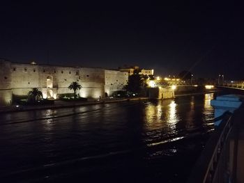 Illuminated buildings by river against sky at night