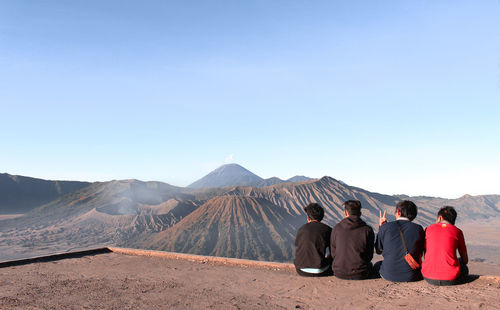 Rear view of friends sitting on mountain against clear sky