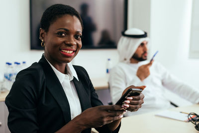 Portrait of smiling businesswoman using smart phone while sitting with colleague at office