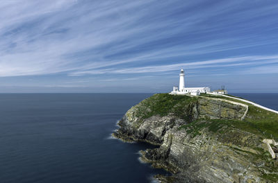 Lighthouse amidst sea and buildings against sky