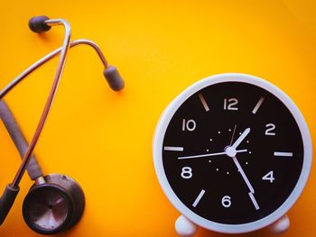 Close-up of alarm clock and stethoscope on yellow background