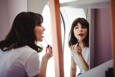 Close-up of young woman applying red lipstick in front of mirror at home