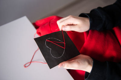 The child's hands make a card with a heart for mother's day with red threads