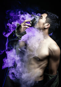 Young man smoking against black background