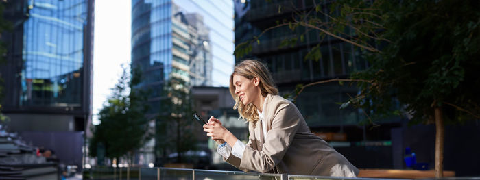 Side view of young woman using mobile phone while standing in city