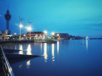 Illuminated city by sea against sky at night