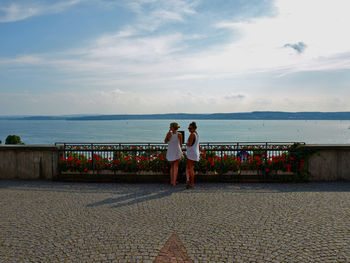 Full length rear view of female friends standing on promenade against sea