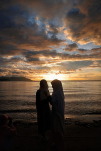 Couple on beach against sky during sunset