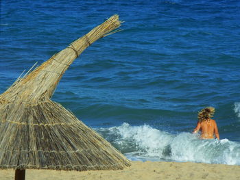 Thatched parasol at beach with naked woman in sea