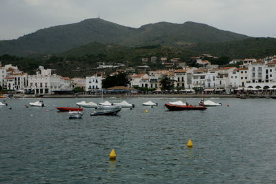 Sailboats moored on sea by buildings in city against sky