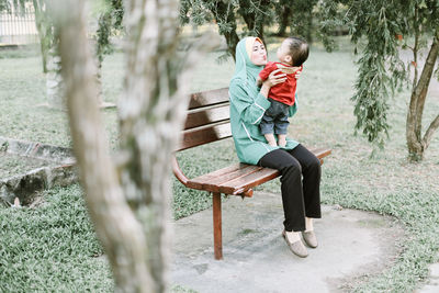 Mother playing with son while sitting on bench at park