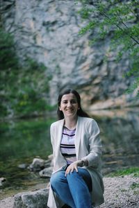 Portrait of smiling woman sitting on rock in forest