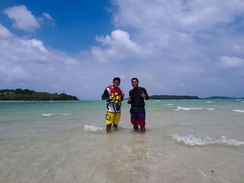 Men gesturing thumbs up while standing in sea against sky during summer