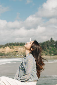 Side view of woman sitting against sky during sunny day