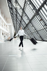 Cheerful woman with purse and suitcase walking in office corridor