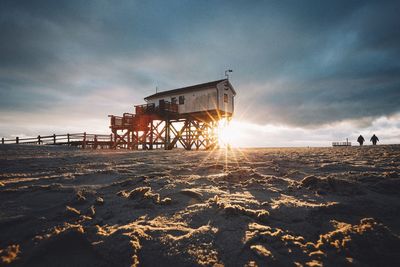 Sun shining on beach hut at sea shore against cloudy sky