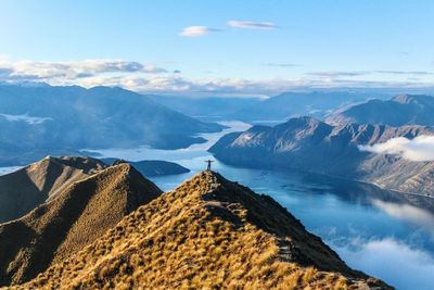 Scenic view of mountains and river with man standing against sky