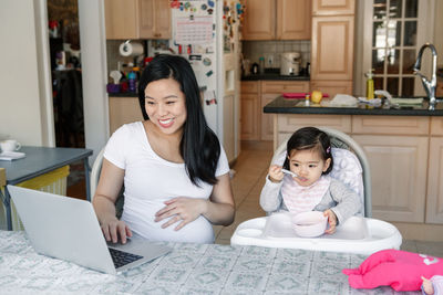 Asian chinese pregnant mother with daughter baby working online from home on internet. 