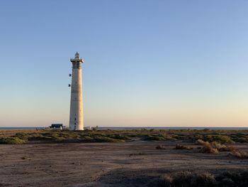 Lighthouse by sea against clear sky during sunset