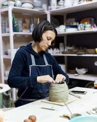 Woman making clay pot on table in workshop
