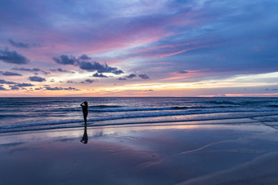 Woman standing on beach against sky during sunset