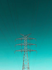 Low angle view of electricity pylon against clear blue sky