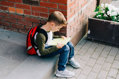 Side view of boy using mobile phone while sitting against wall