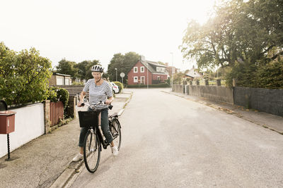 Senior woman with bicycle on road against house