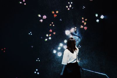 Rear view of woman standing against illuminated lights at night